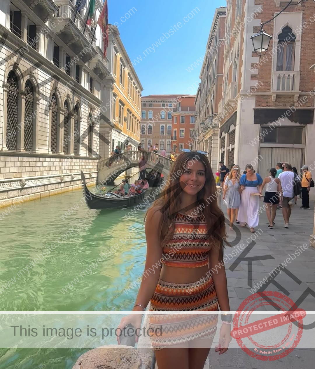 emma-deana-spain-emmadeana-15437 Emma Deana, track and field star from Spain smiles in a patterned dress by a Venice canal with people, gondola, and historic buildings.
