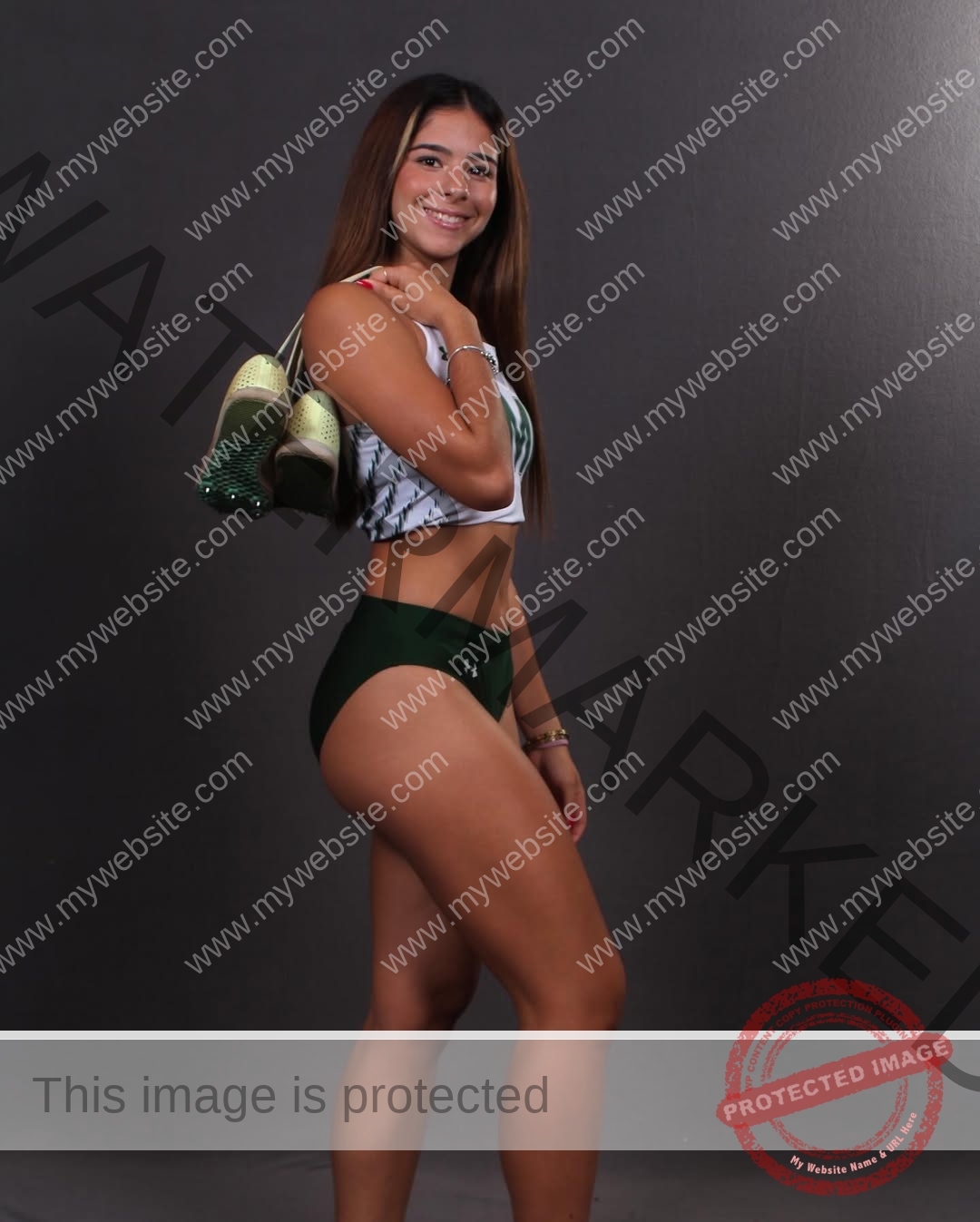 emma-deana-spain-emmadeana-15444 Emma Deana, track and field star from Spain, poses sideways in sports gear with green shoes over her shoulder, smiling confidently.