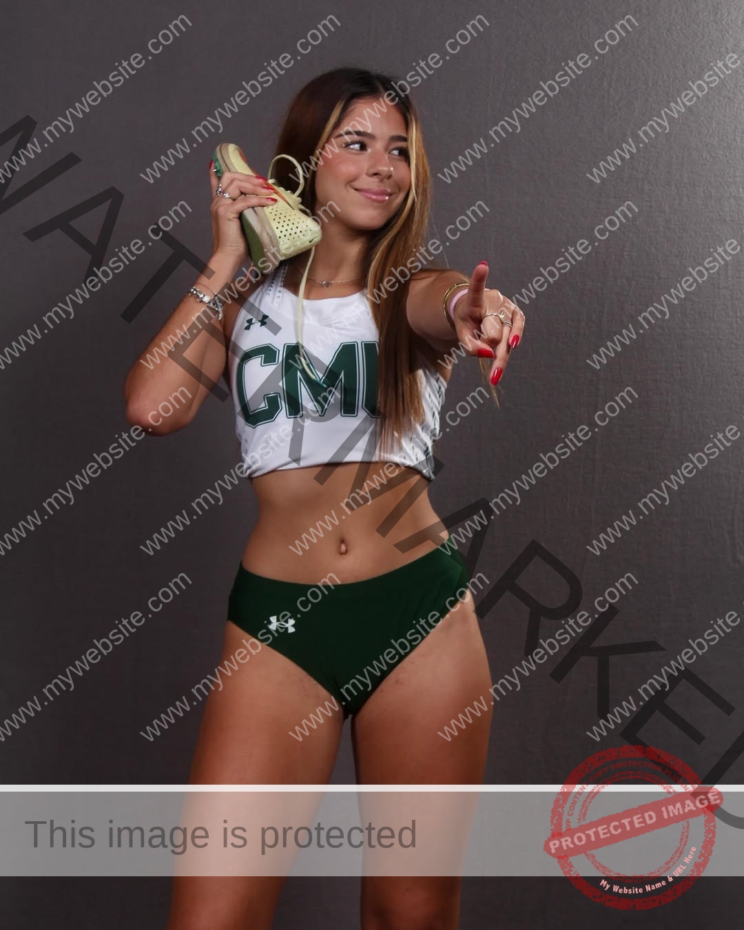 emma-deana-spain-emmadeana-15446 Emma Deana, track and field star from Spain, in a CMU uniform, holds a shoe like a phone and points forward, smiling.