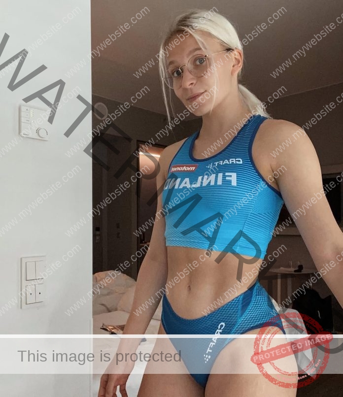 Jenna Kokkonen, track and field star from Finland, stands in a blue FINLAND uniform, blonde hair and glasses, looking at camera.