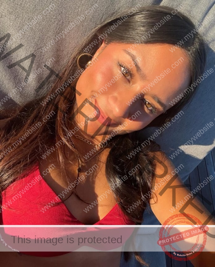 Keira McGregor, track and field star from Australia, with long dark hair in a red top, smiles on a gray cushion in bright sunlight.
