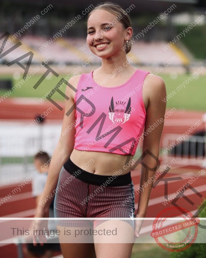 Khrystyna Fedushchak, track and field star from Ukraine, smiles in a pink crop top and striped shorts on a track with stadium seats behind.