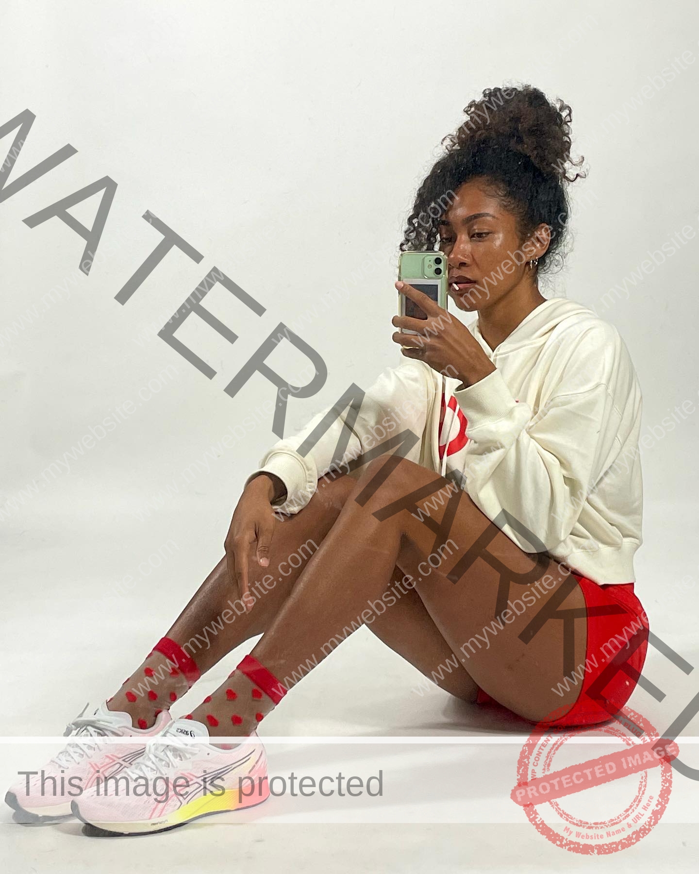kristina-knott-philippines-knottyourcheese-x-18308 Kristina Knott, track and field star from Philippines, sits on the floor in a white hoodie and red shorts, taking a mirror selfie.