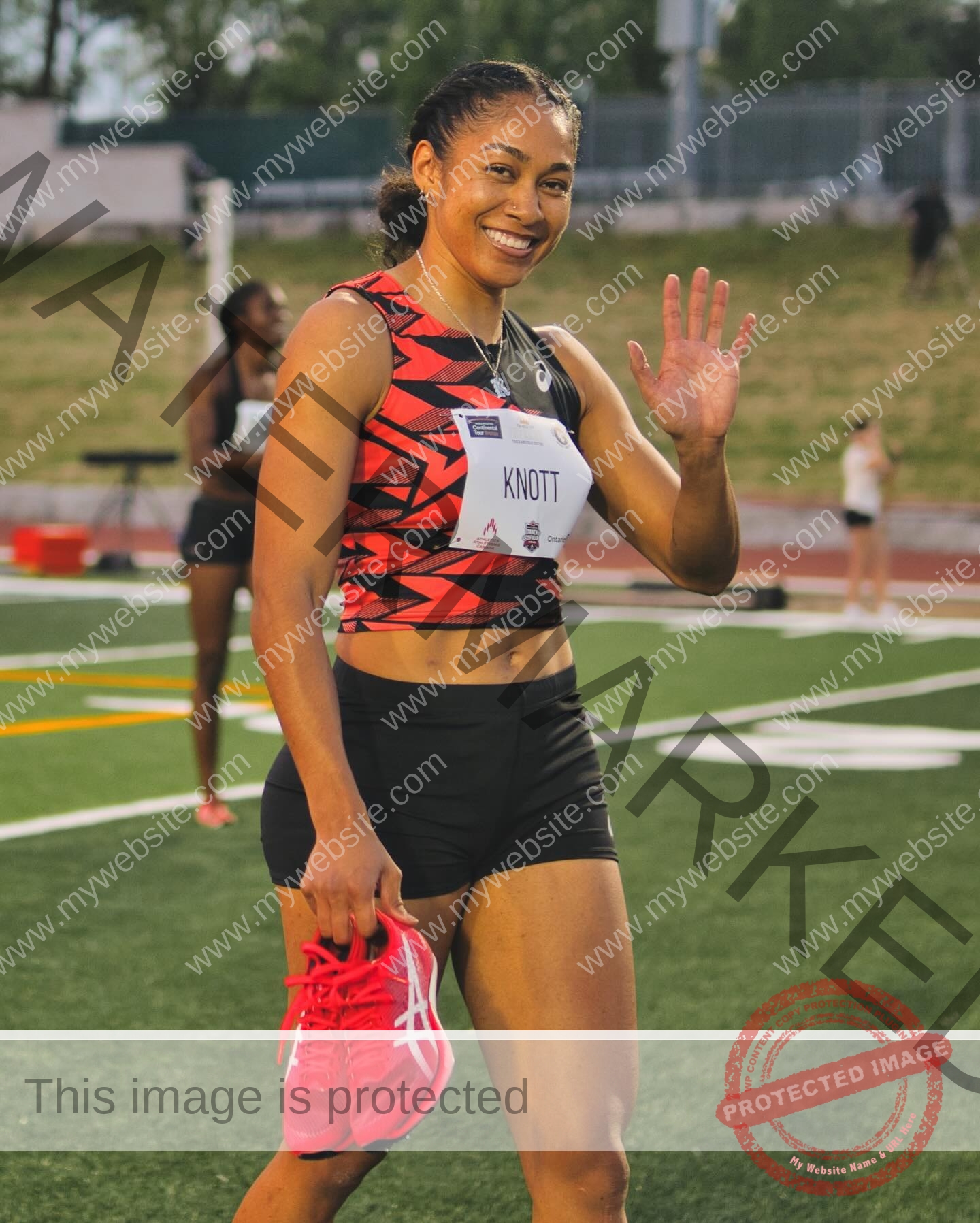 kristina-knott-philippines-knottyourcheese-x-18540 Kristina Knott, track and field star from Philippines, smiles and waves on a track, holding red shoes; another runner in background.