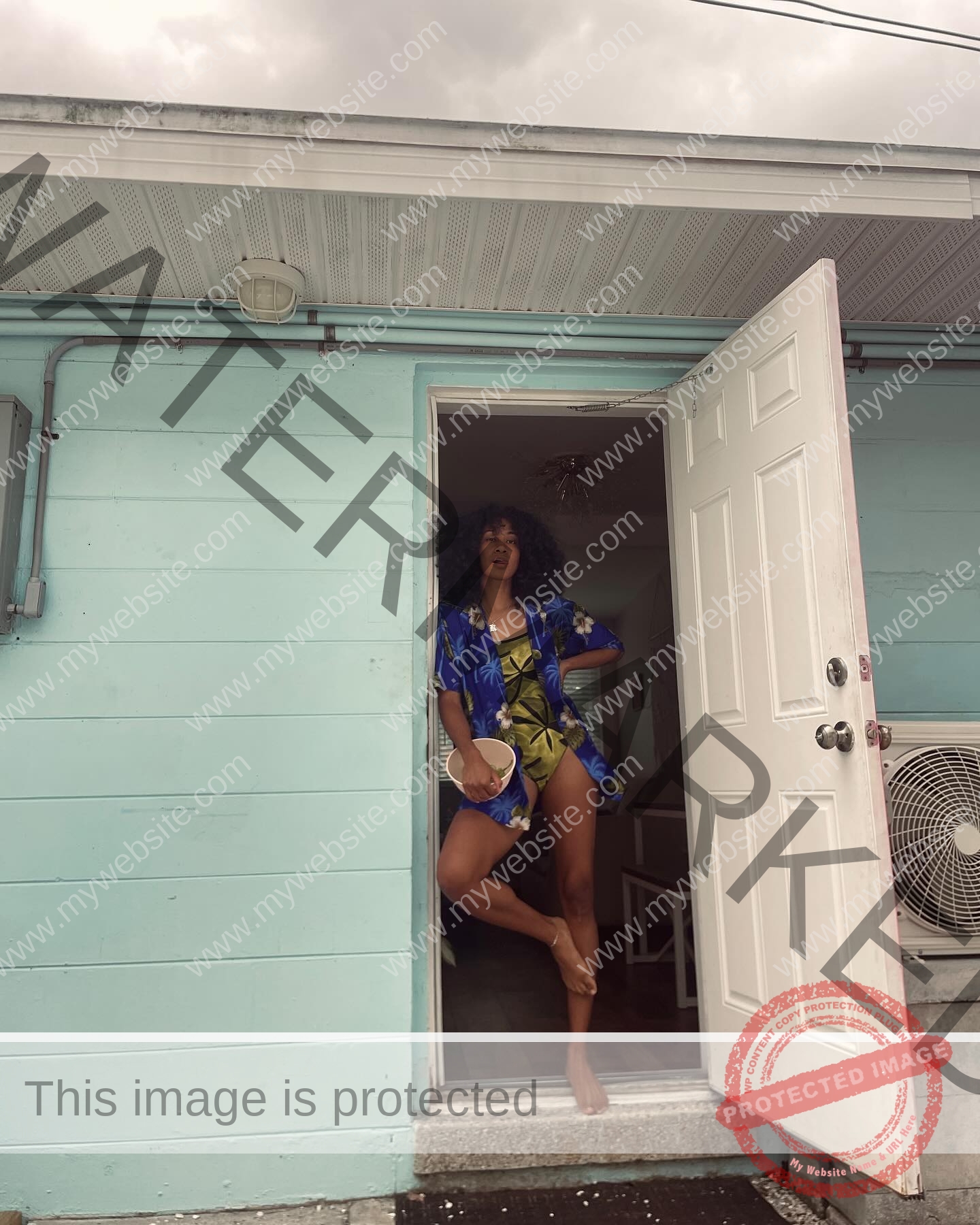 kristina-knott-philippines-knottyourcheese-x-18544 Kristina Knott, track and field star from Philippines, in a tropical shirt stands barefoot by a blue door holding a drink under cloudy skies.