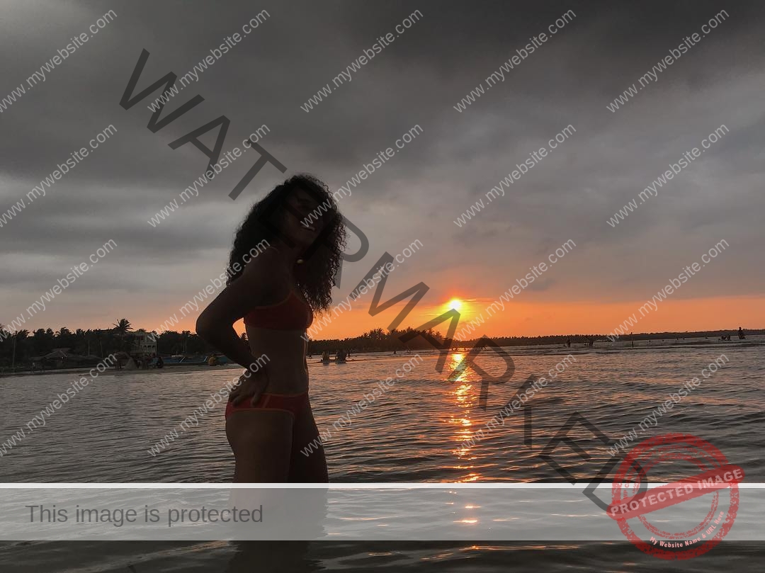 kristina-knott-philippines-knottyourcheese-x-18646 Kristina Knott, track and field star from Philippines, stands in a bikini in shallow water at sunset, smiling with hands on hips.