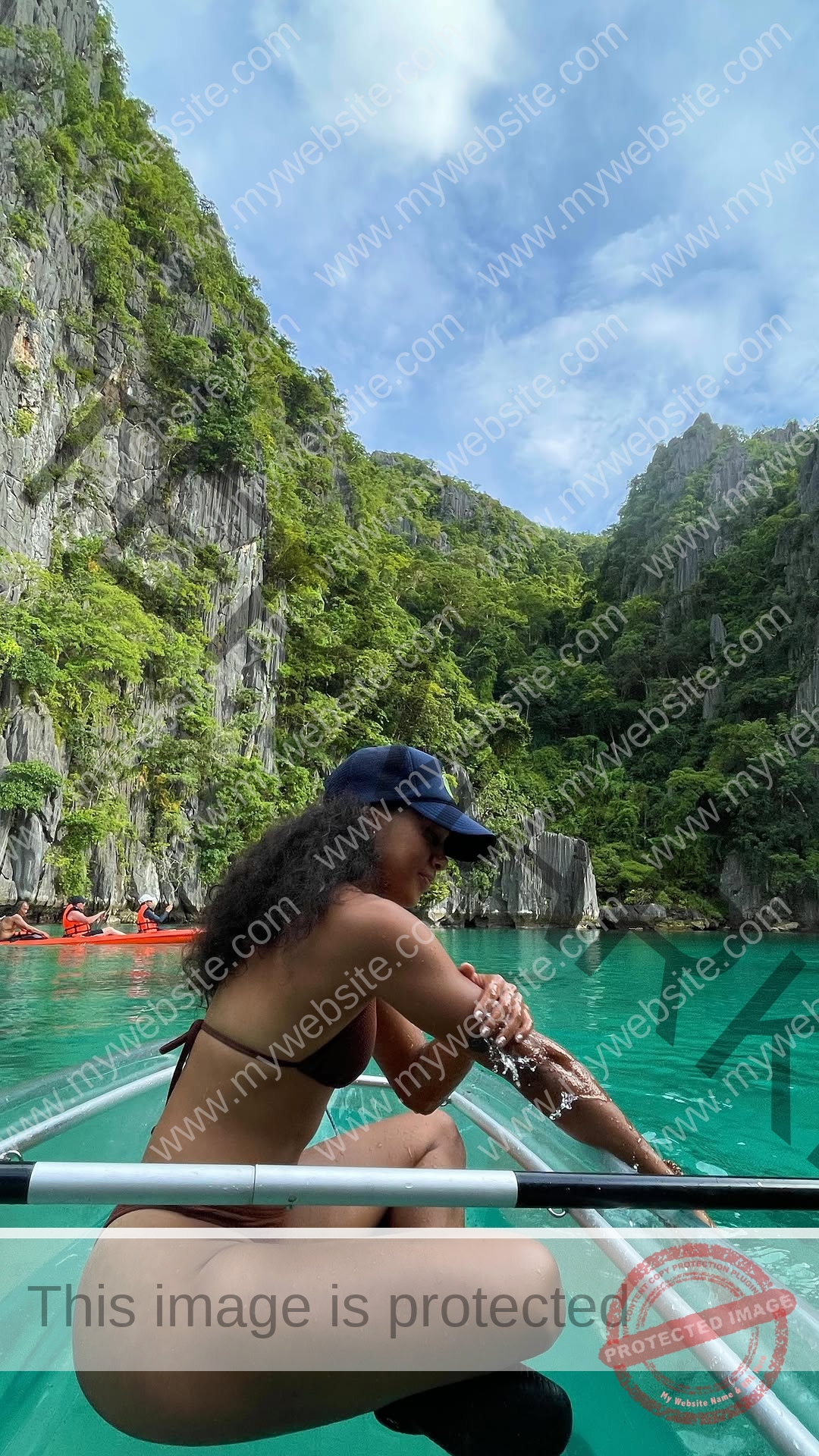 kristina-knott-philippines-knottyourcheese-x-19125 Kristina Knott, track and field star from Philippines, in a black bikini and navy cap sits in a clear kayak on turquoise water.