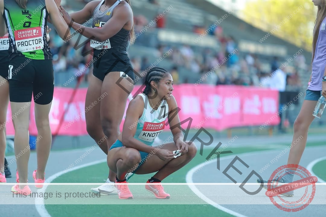 kristina-knott-philippines-knottyourcheese-x-19150 Kristina Knott, track and field star from Philippines, squats on a track in sportswear as others and a crowd with pink banners watch.