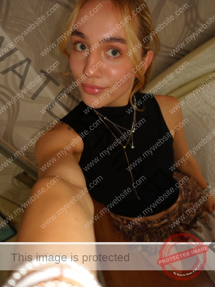 Liza Zemlianikina, track and field star from Russia, with blonde hair in black sleeveless top, smiles softly taking a selfie indoors.