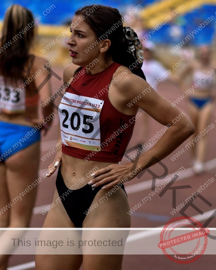 Marianna Bakosova, track and field star from Russia stands on the track in a red crop top 205, hands on hips; others behind.