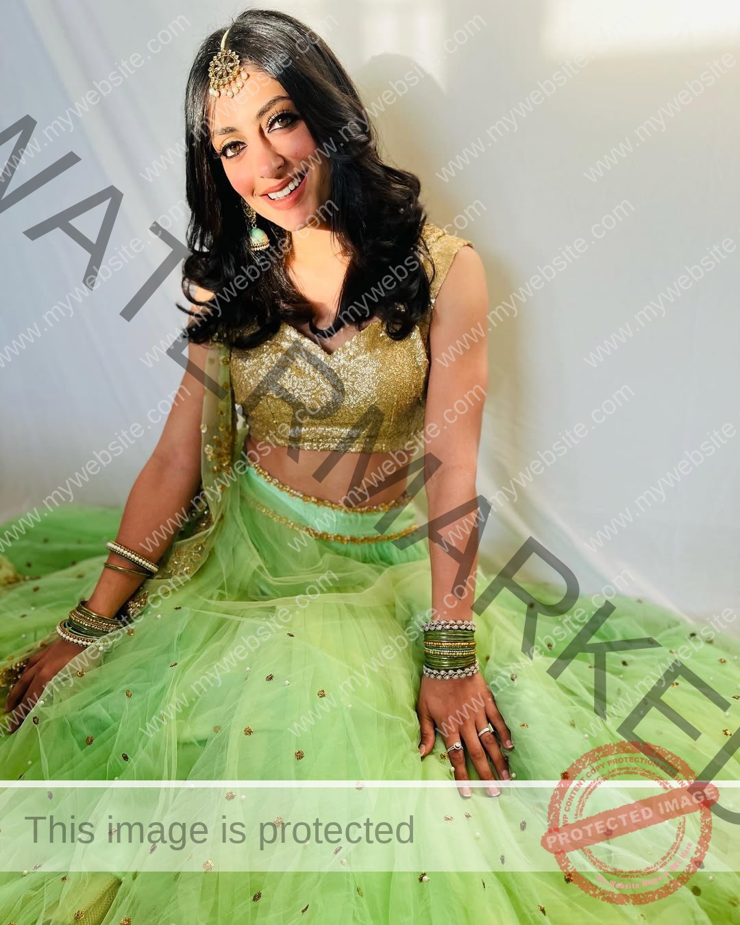niharika-vashisht-india-niharika.vashhisht-05568 Niharika Vashisht, track and field star from India, sits on the floor in a gold blouse and green lehenga, smiling, against white.