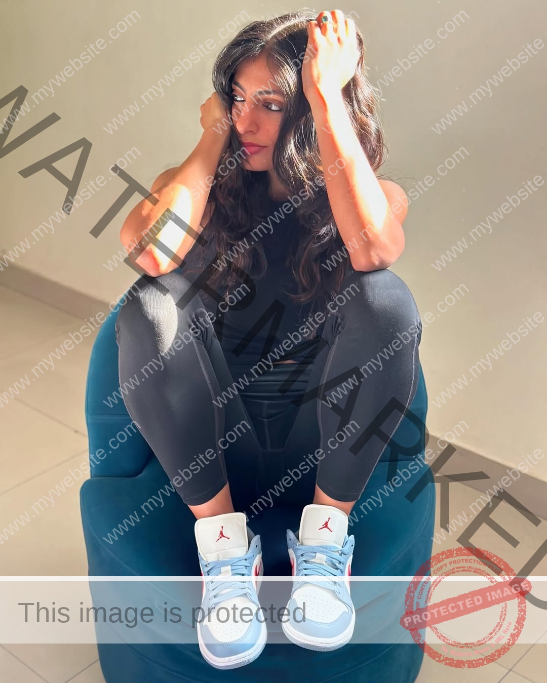 niharika-vashisht-india-niharika.vashhisht-05681 Niharika Vashisht, track and field star from India, sits on a blue chair hugging her knees, sunlight on her face and arm.