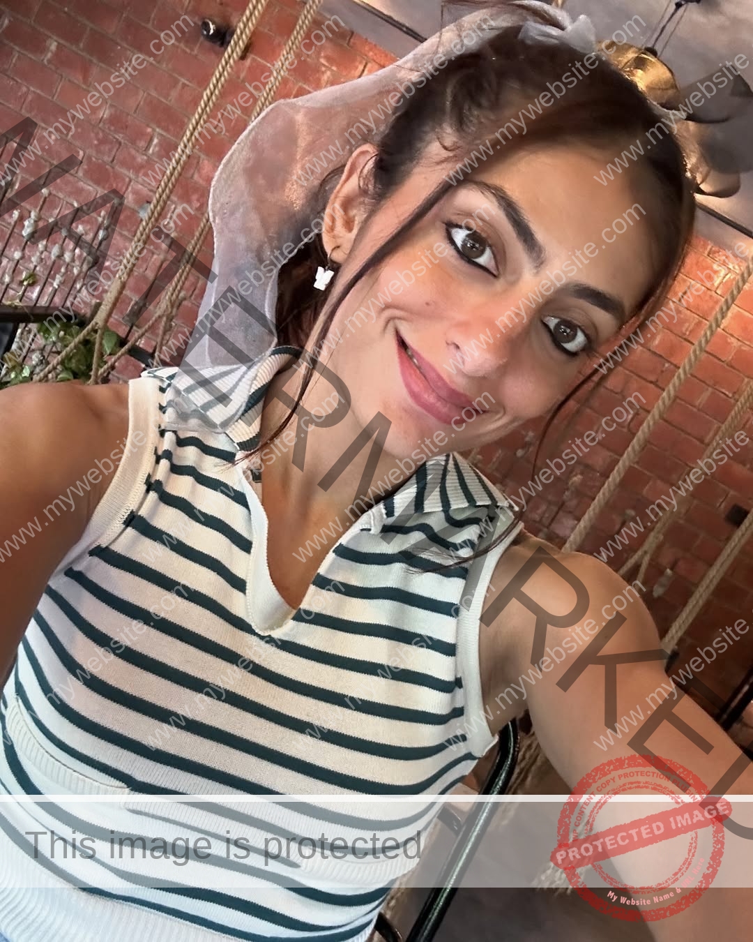 niharika-vashisht-india-niharika.vashhisht-05700 Niharika Vashisht, track and field star from India smiles, taking a selfie in a white striped top indoors with brick walls and swings.