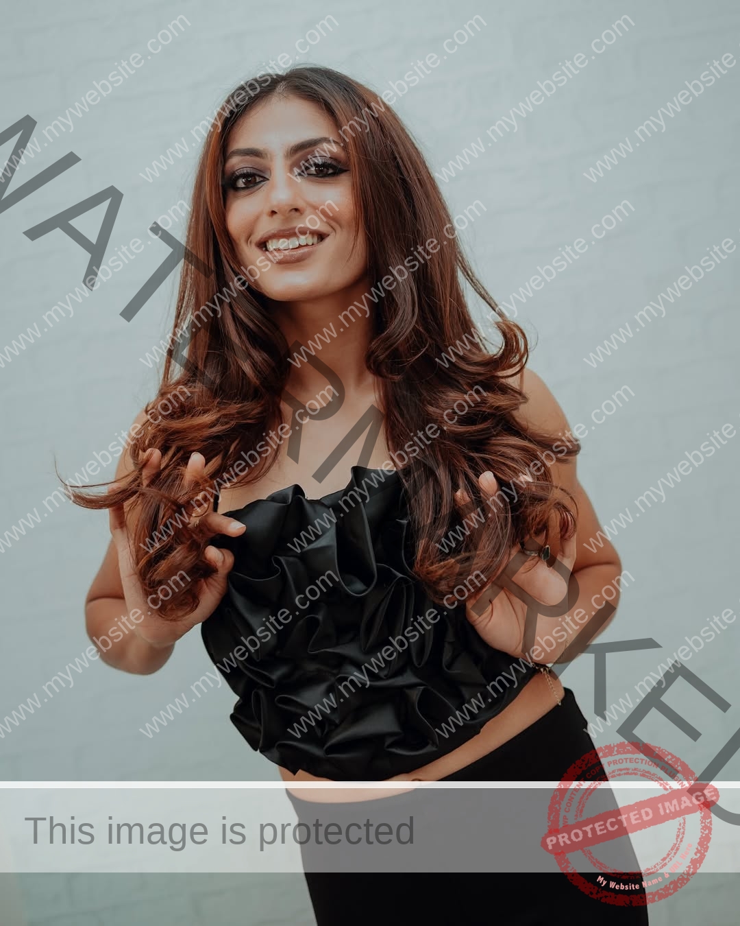 niharika-vashisht-india-niharika.vashhisht-05744 Niharika Vashisht, track and field star from India, with long brown hair in a black ruffled strapless top and pants, smiles holding her hair.