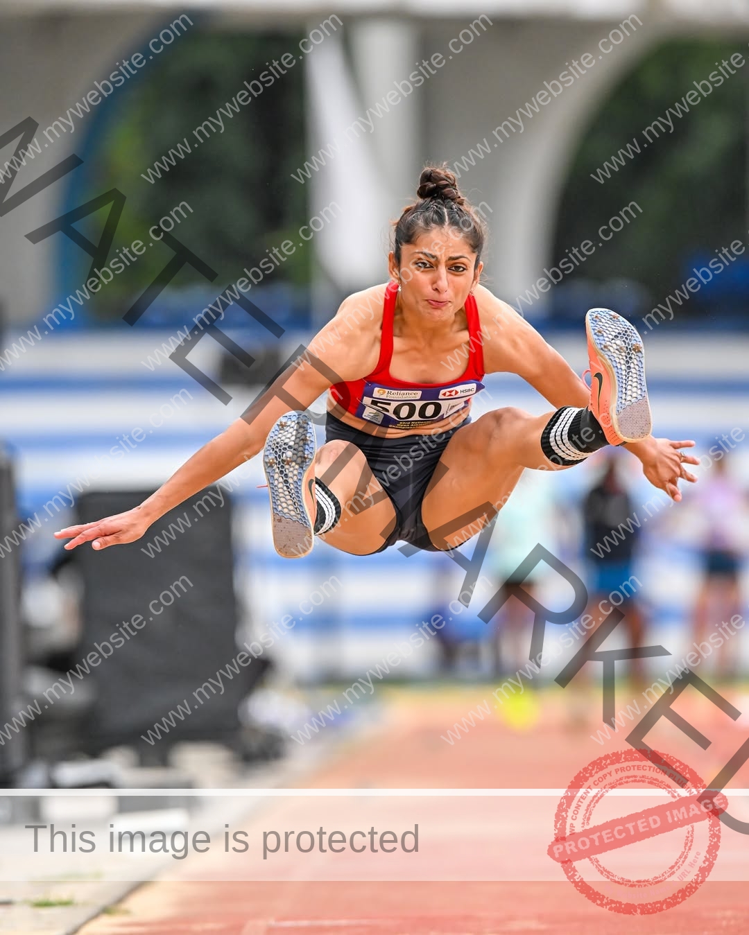 niharika-vashisht-india-niharika.vashhisht-05826 Niharika Vashisht, track and field star from India, leaps mid-air in red and black long jump gear, bib 500; blurred track behind.