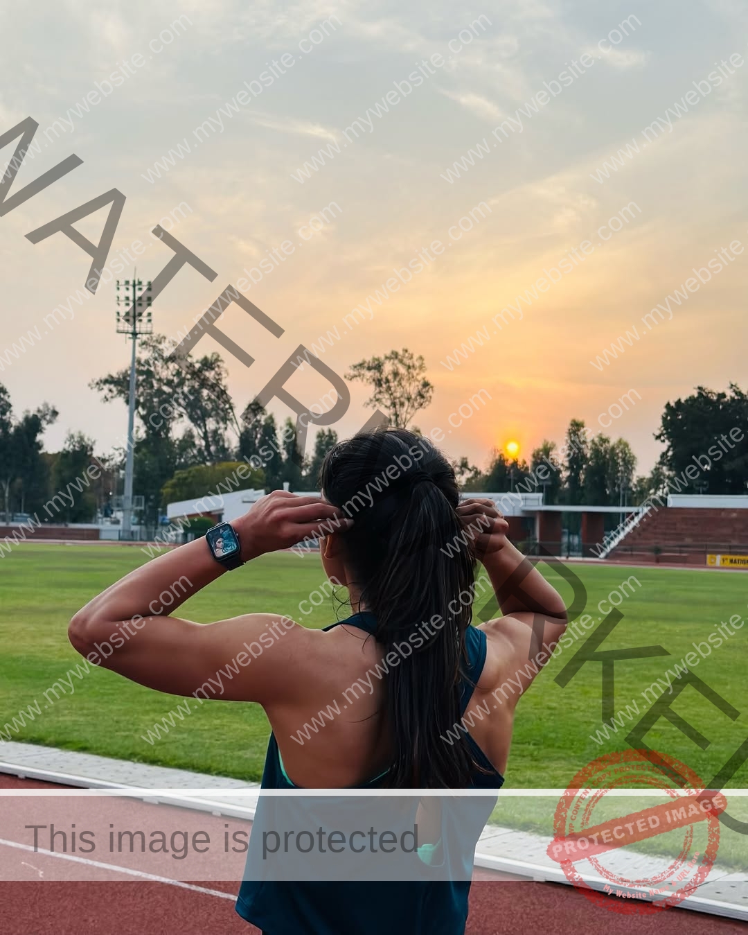 niharika-vashisht-india-niharika.vashhisht-05868 Niharika Vashisht, track and field star from India, stands on a sunset track adjusting her ponytail, facing an empty stadium.
