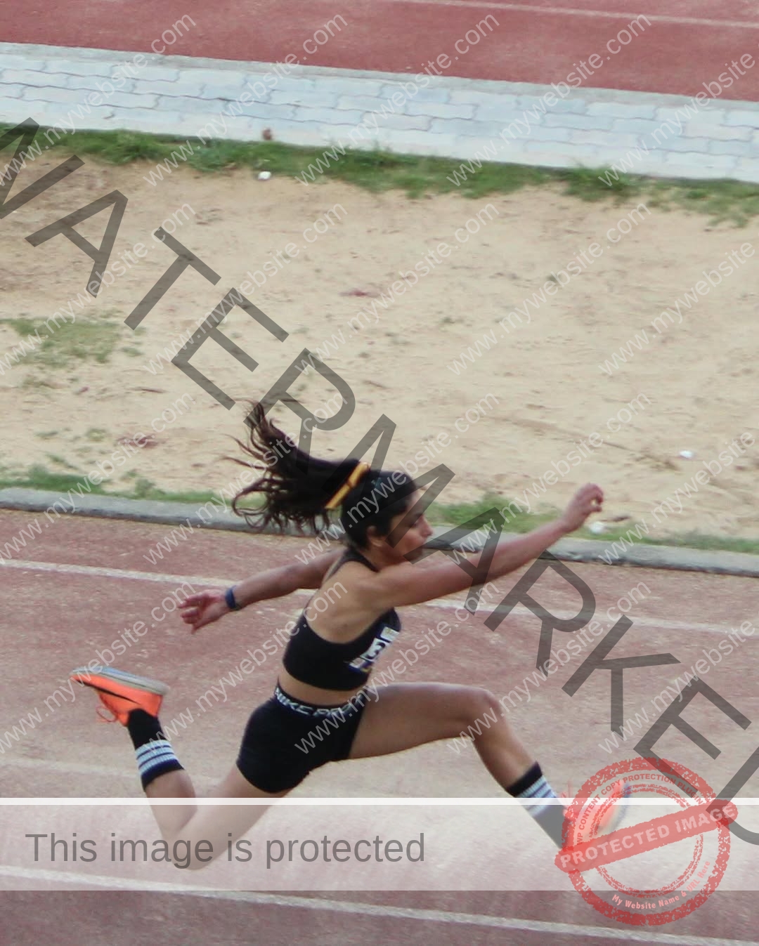 niharika-vashisht-india-niharika.vashhisht-05893 Niharika Vashisht, track and field star from India, in black sportswear and orange shoes mid-air long jumping on an outdoor track.