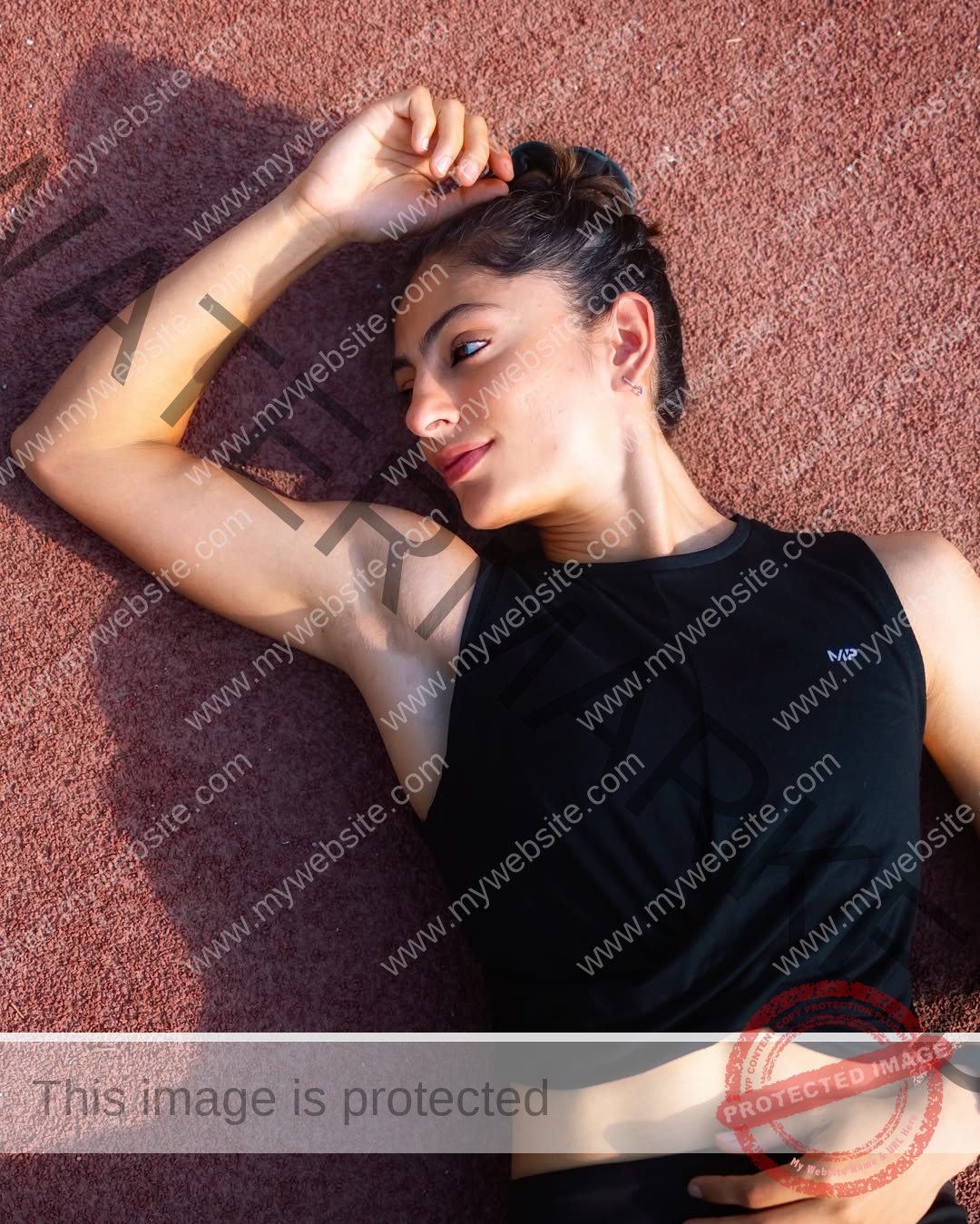 niharika-vashisht-india-niharika.vashhisht-05931 Niharika Vashisht, track and field star from India, in a black sleeveless top lies on a red surface, arm raised, smiling softly.