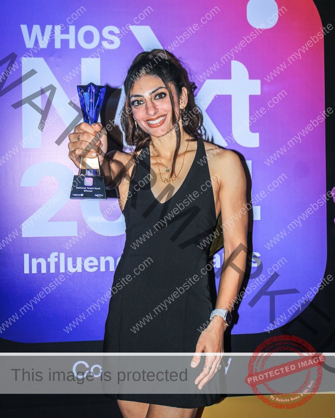 niharika-vashisht-india-niharika.vashhisht-05937 Niharika Vashisht, track and field star from India, in a sleeveless black dress smiles holding a blue trophy at Whos Next 2024.