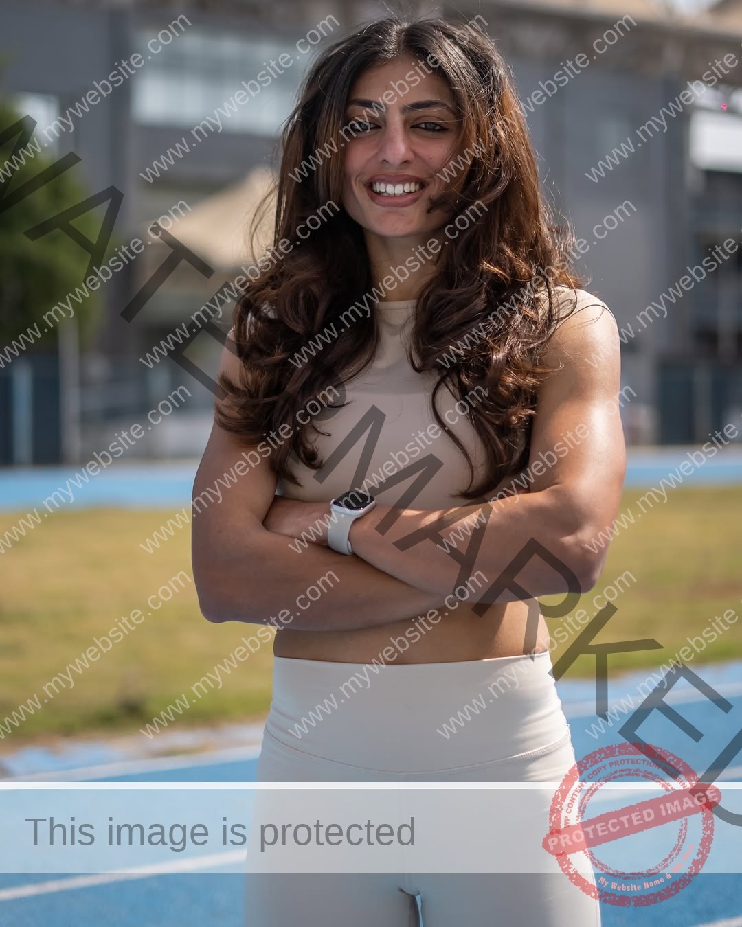 niharika-vashisht-india-niharika.vashhisht-06006 Niharika Vashisht, track and field star from India, stands on a blue track in light athletic wear, arms crossed, smiling confidently.