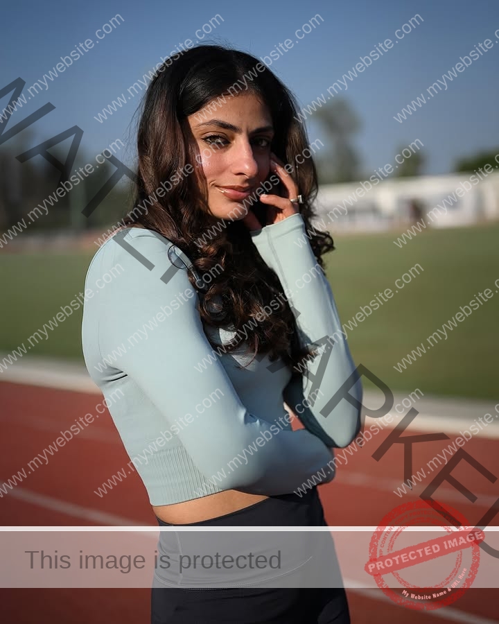 niharika-vashisht-india-niharika.vashhisht-06015 Niharika Vashisht, track and field star from India, stands on a running track in blue top and dark leggings, smiling slightly.