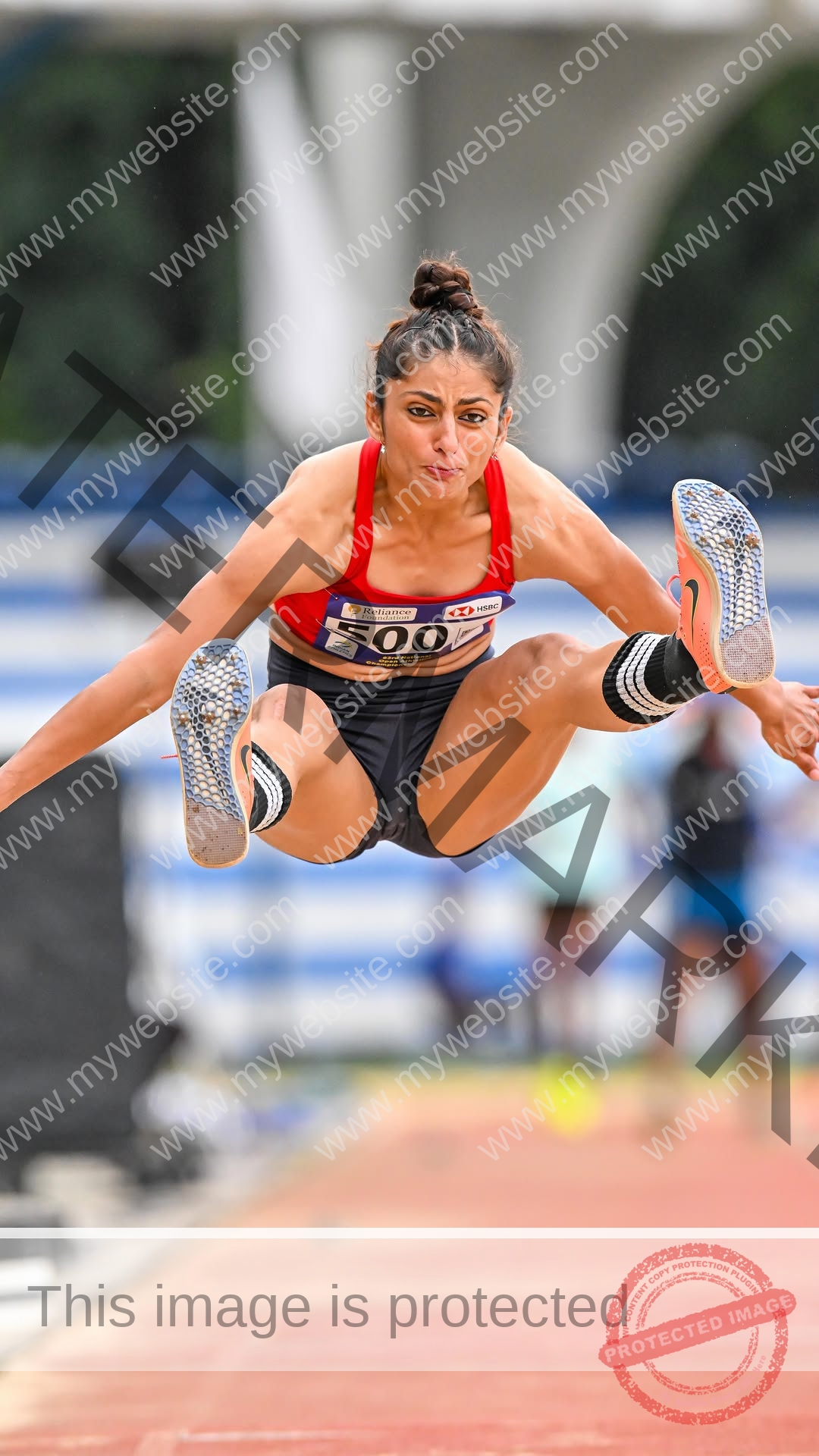 niharika-vashisht-india-niharika.vashhisht-06038 Niharika Vashisht, track and field star from India, in mid-air during a long jump, red top, black shorts, arms outstretched.