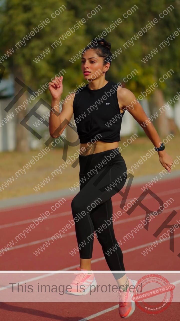 niharika-vashisht-india-niharika.vashhisht-06053 Niharika Vashisht, track and field star from India, jogs on a red outdoor track in black top, leggings, pink shoes, smartwatch.