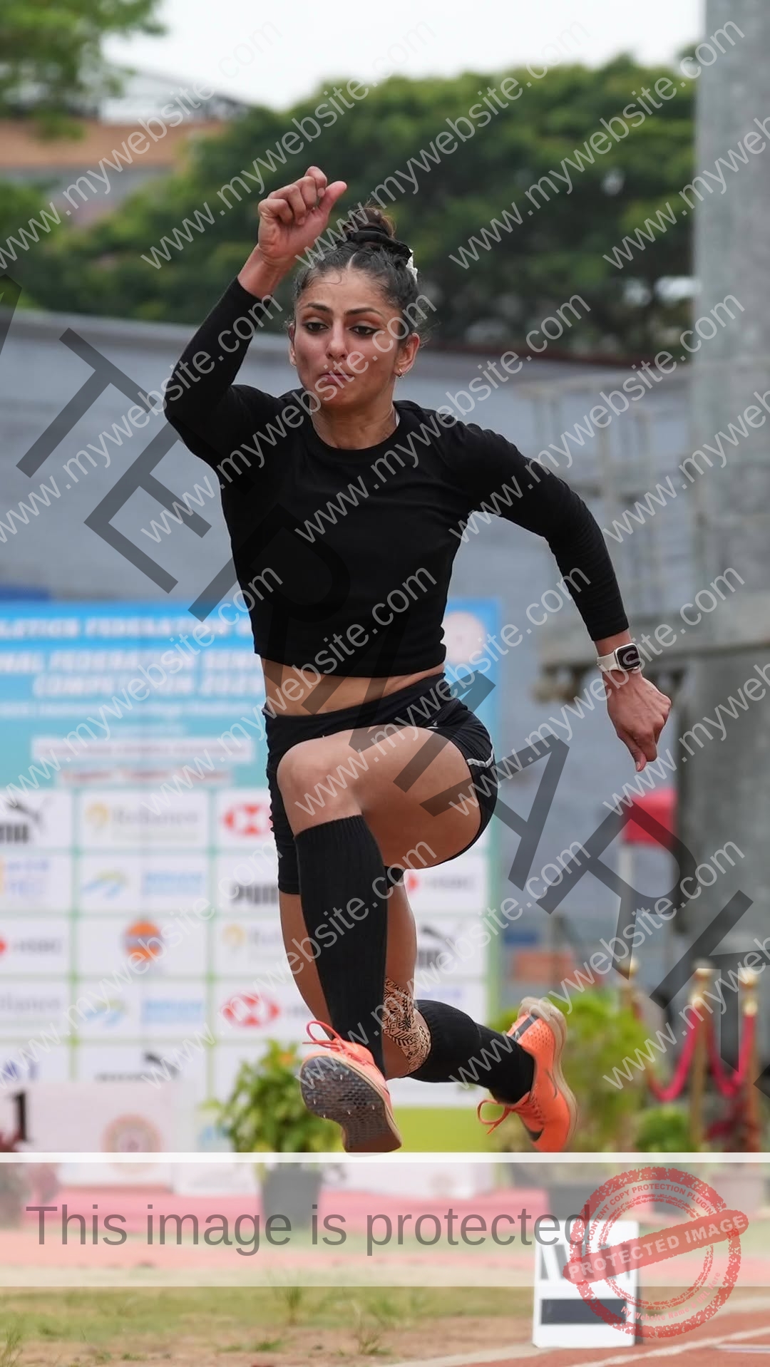 niharika-vashisht-india-niharika.vashhisht-06081 Niharika Vashisht, track and field star from India, in black sportswear and orange shoes, leaps mid-air at a long jump event.