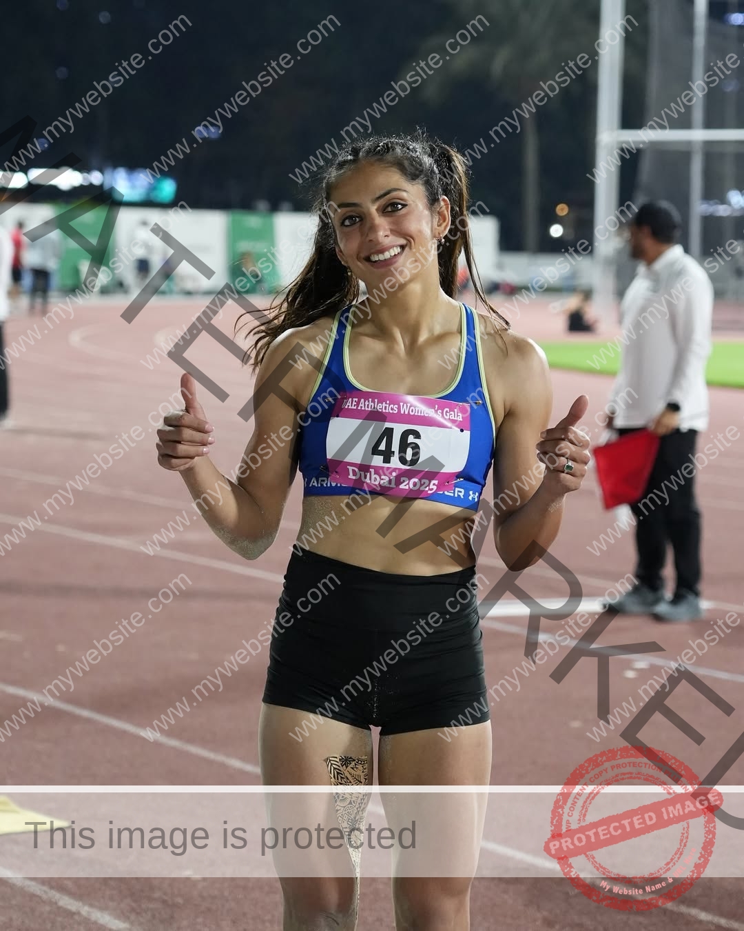 niharika-vashisht-india-niharika.vashhisht-06100 Niharika Vashisht, track and field star from India, in a blue top and black shorts, smiles with thumbs up on the running track.