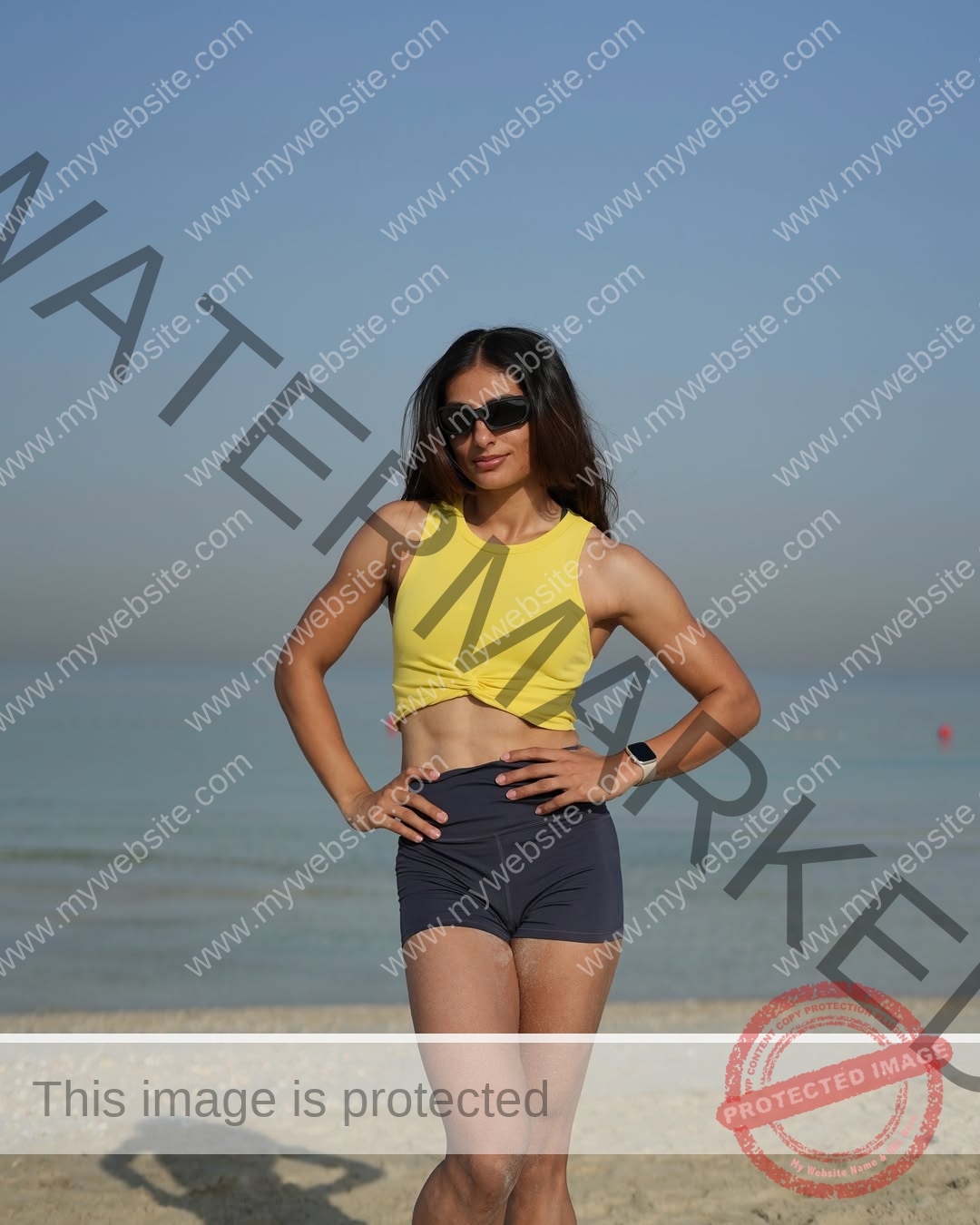 niharika-vashisht-india-niharika.vashhisht-06104 Niharika Vashisht, track and field star from India, stands on a beach in a yellow crop top and shorts, sea and sky behind her.