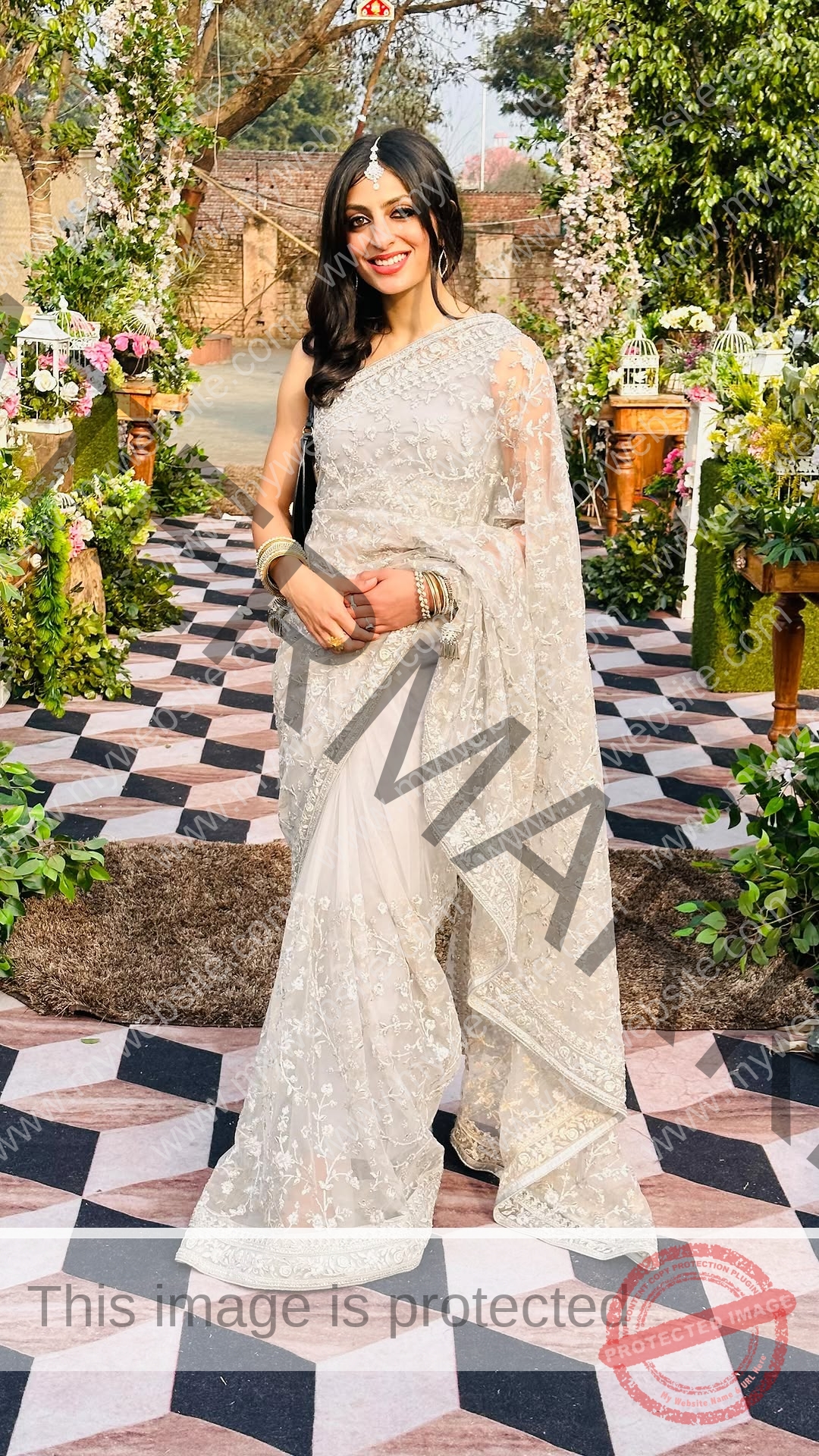 niharika-vashisht-india-niharika.vashhisht-06175 Niharika Vashisht, track and field star from India, wears an elegant embroidered white saree and smiles on a walkway amid greenery.