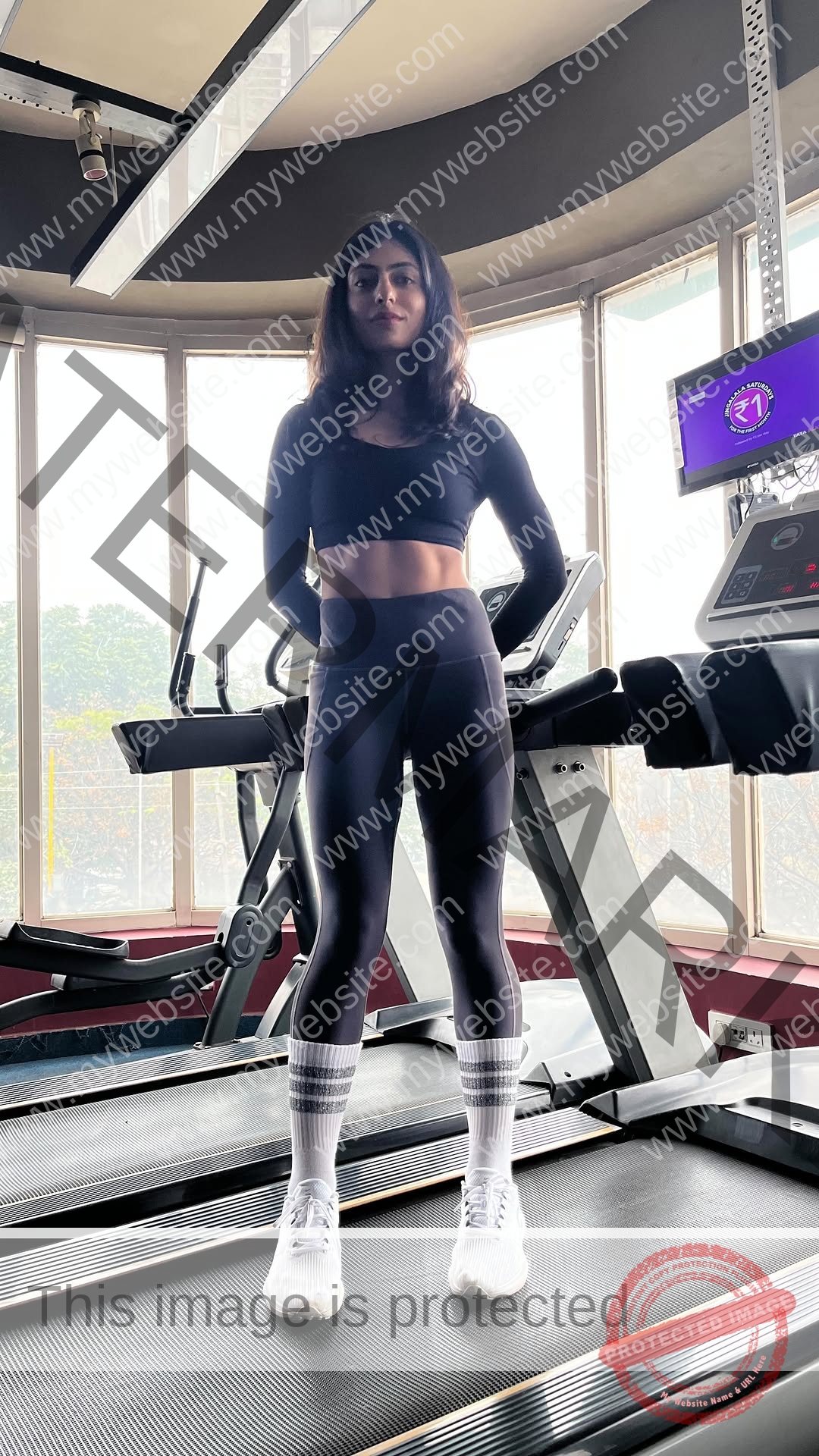 niharika-vashisht-india-niharika.vashhisht-06182 Niharika Vashisht, track and field star from India, stands on a treadmill in black athletic wear with bright gym windows behind her.