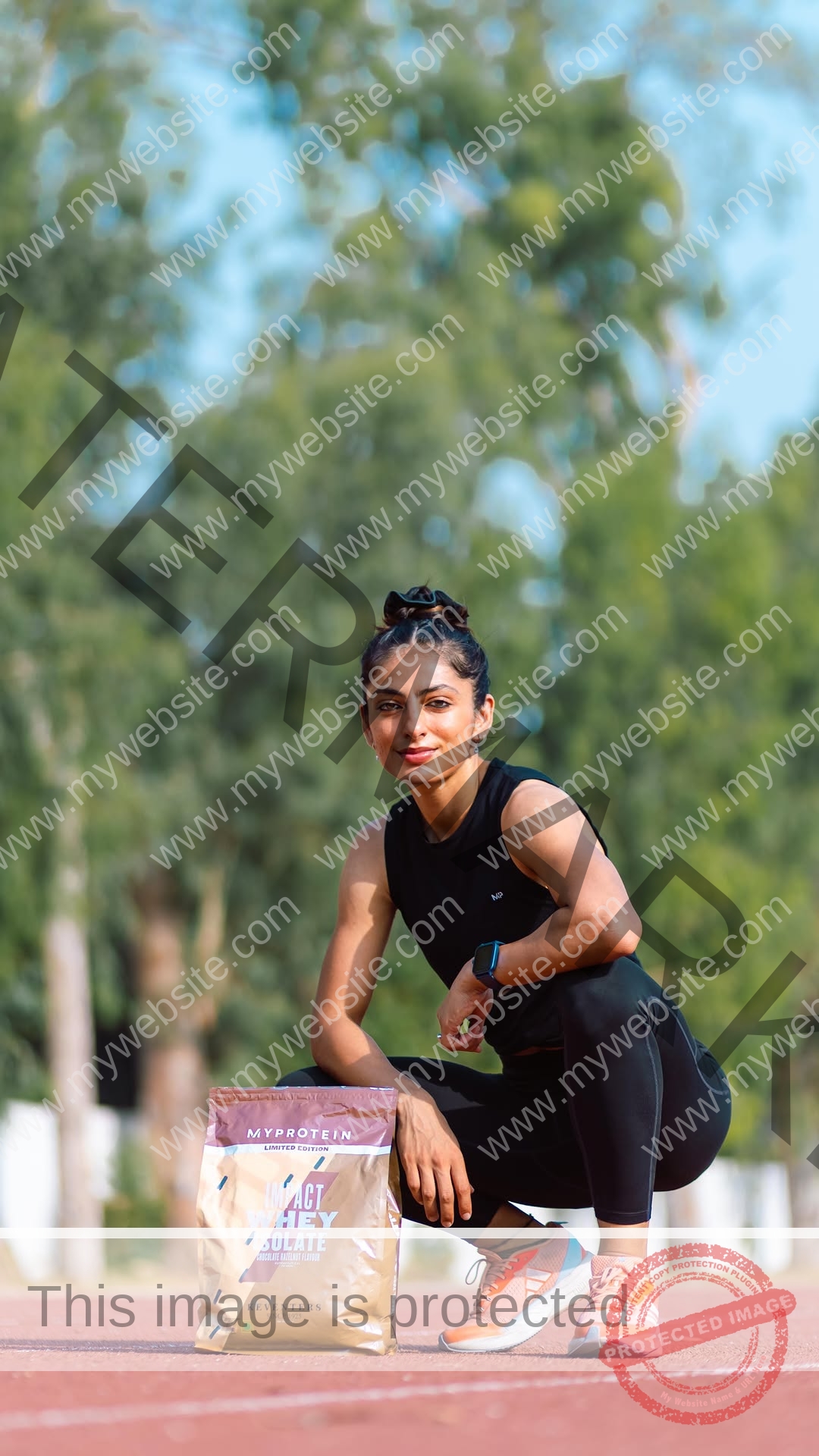niharika-vashisht-india-niharika.vashhisht-06189 Niharika Vashisht, track and field star from India, squats on a track with MyProtein Impact Whey Isolate in front; greenery behind.
