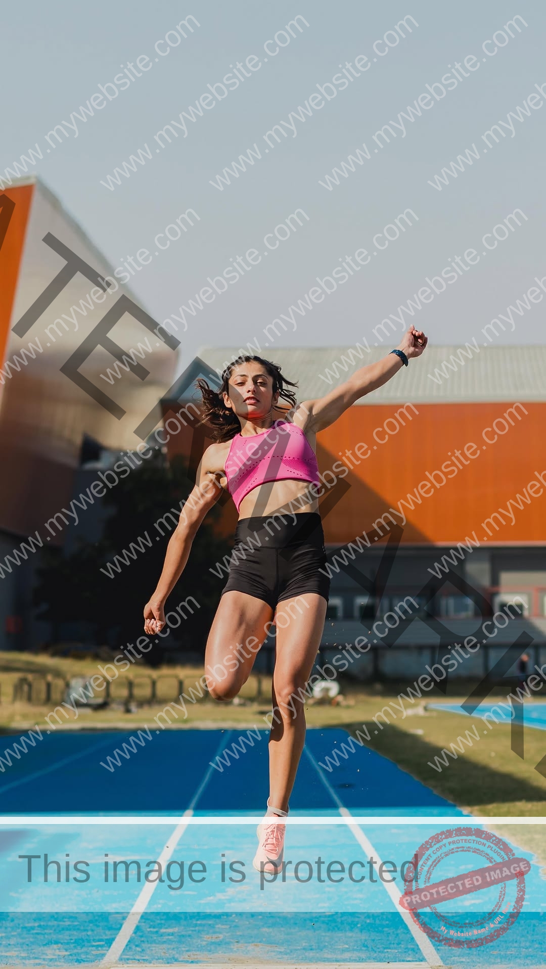 niharika-vashisht-india-niharika.vashhisht-06194 Niharika Vashisht, track and field star from India, leaps mid-air in a pink sports bra and black shorts on a blue track.