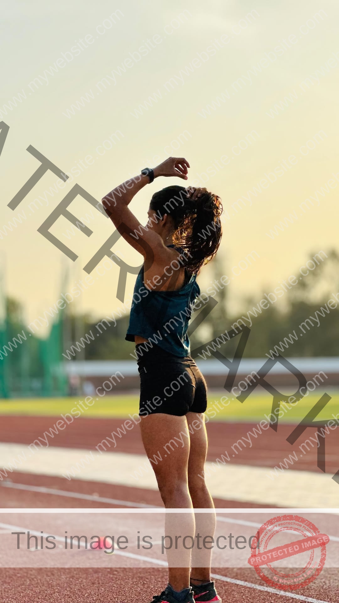 niharika-vashisht-india-niharika.vashhisht-06196 Niharika Vashisht, track and field star from India, stands on a running track at sunset in sporty attire, adjusting her hair.