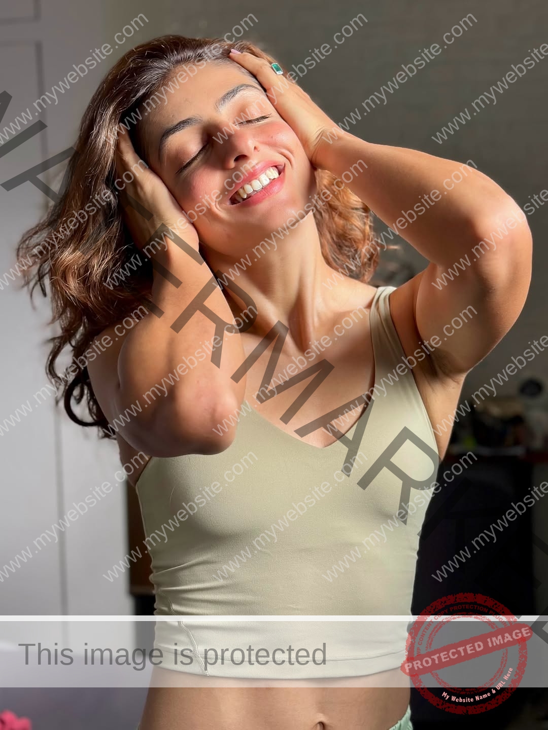 niharika-vashisht-india-niharika.vashhisht-06243 Niharika Vashisht, track and field star from India beams joyfully, eyes closed, hands in wavy hair, beige top in sunlit room.