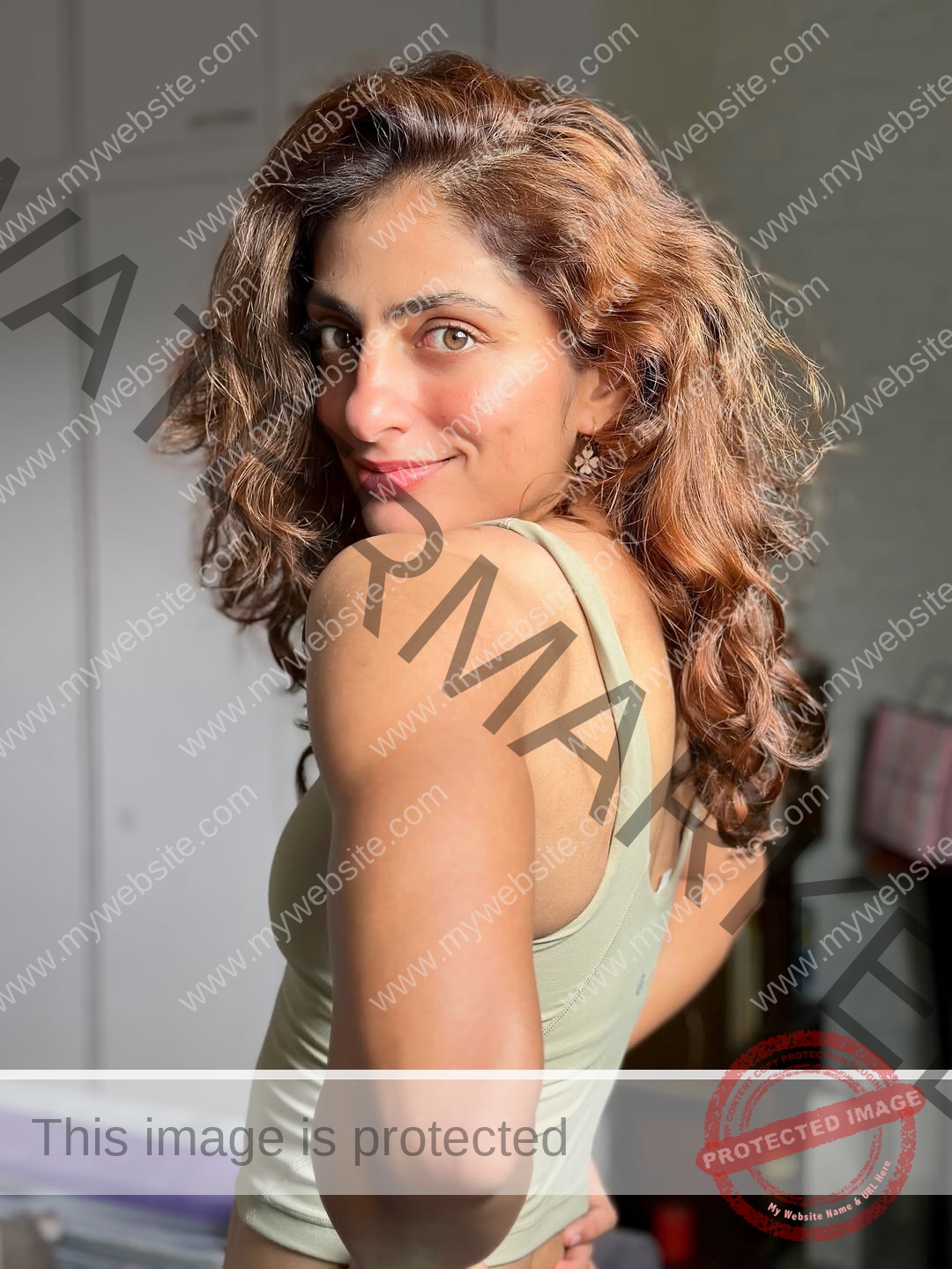 niharika-vashisht-india-niharika.vashhisht-06245 Niharika Vashisht, track and field star from India, with wavy brown hair smiles indoors in a sunlit room, wearing a green sleeveless top.