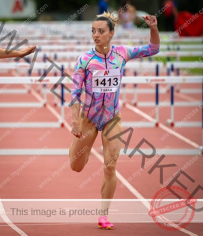 Nikol Andonova, track and field star from Bulgaria, in a colorful leotard and pink shoes, finishes a hurdle race arm raised.