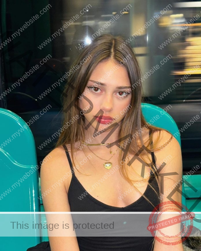 Norma Grezio, track and field star from Italy, with long brown hair and black tank top sits on teal seat in a moving vehicle.