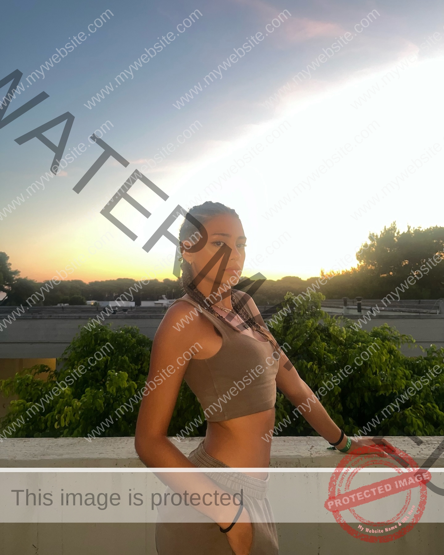 norma-grezio-italy-norma.grezio-u18-xx-07573 Norma Grezio, track and field star from Italy, with braids poses on a balcony at sunset in a tan crop top and pants.