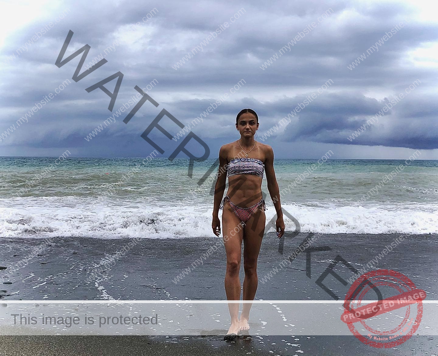 polina-tkalich-russia-p_a_tkalich-10616 Polina Tkalich, track and field star from Russia, in a patterned bikini walks barefoot on wet sand by waves under a dramatic sky.