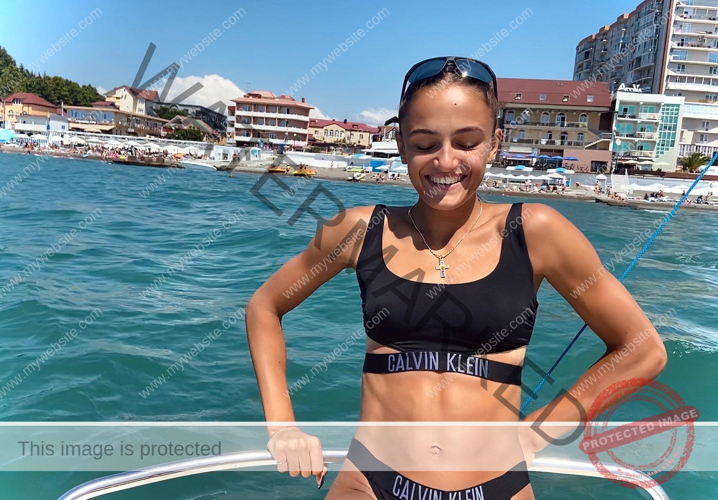 polina-tkalich-russia-p_a_tkalich-10632 Polina Tkalich, track and field star from Russia, in a black Calvin Klein bikini smiles on a boat with blue water and buildings behind.