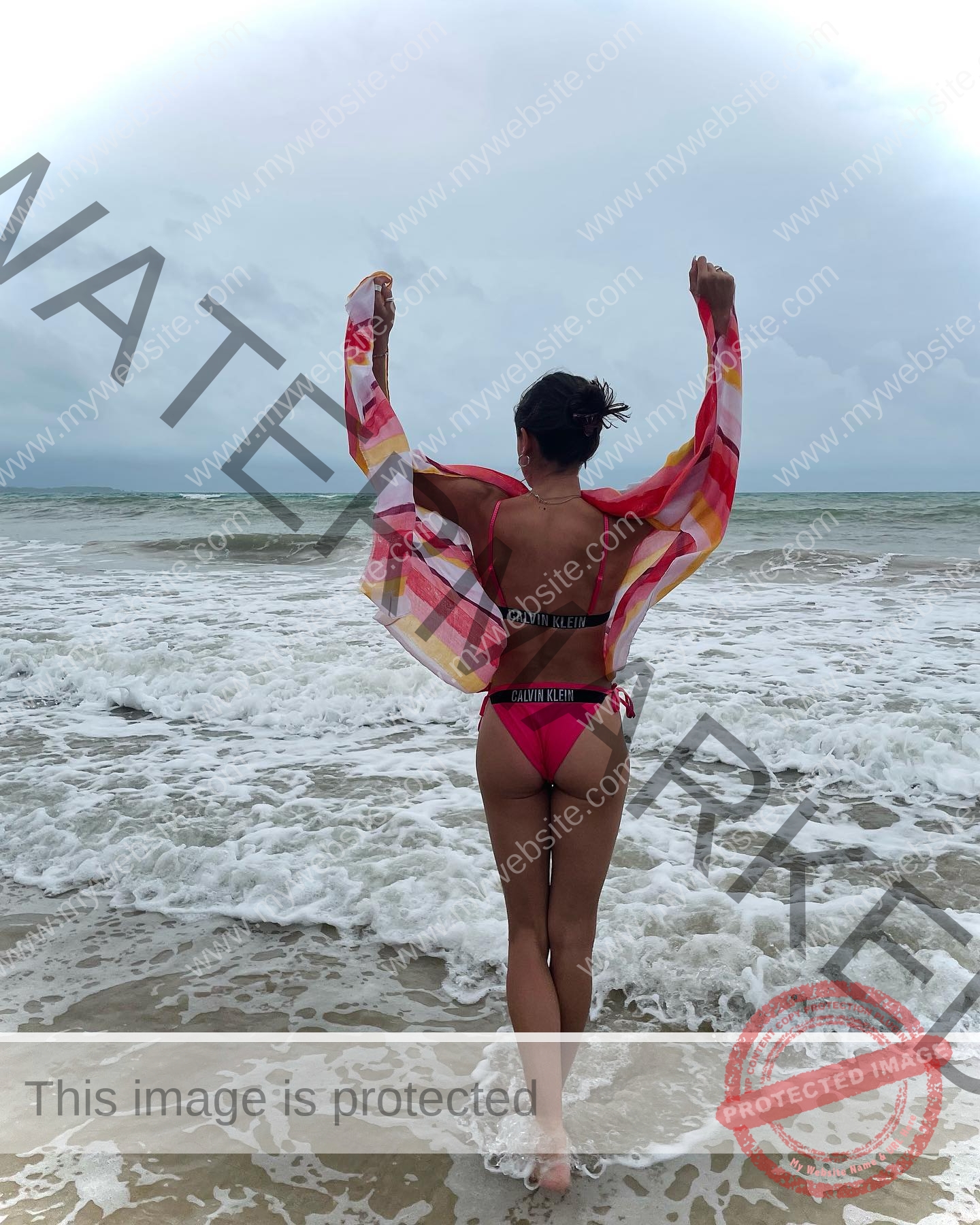 polina-tkalich-russia-p_a_tkalich-10996 Polina Tkalich, track and field star from Russia, stands at the shore in a pink bikini, arms up with a striped cover-up by the sea.