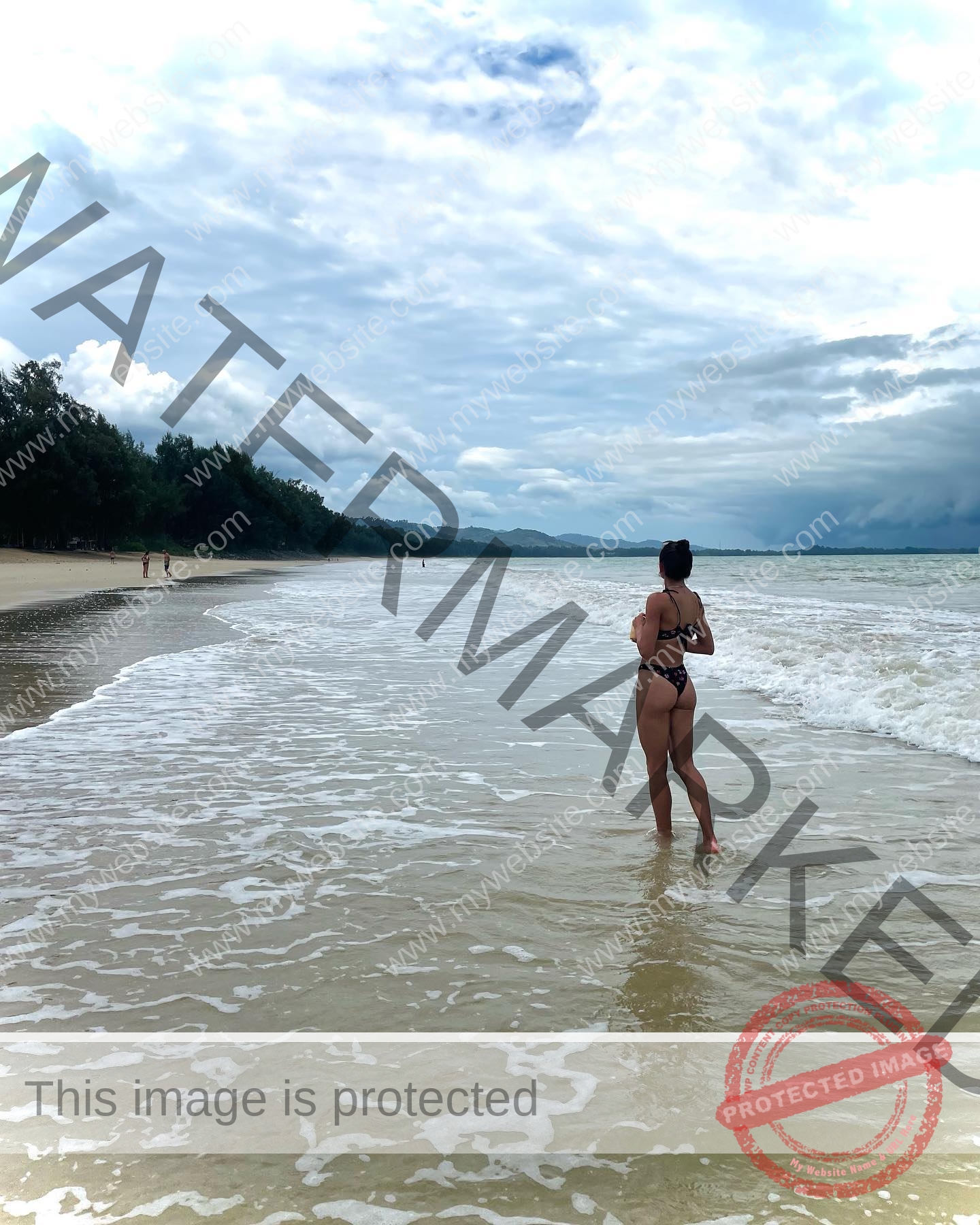 polina-tkalich-russia-p_a_tkalich-10997 Polina Tkalich, track and field star from Russia, stands in a black bikini in shallow ocean water facing a cloudy horizon; trees line the shore.