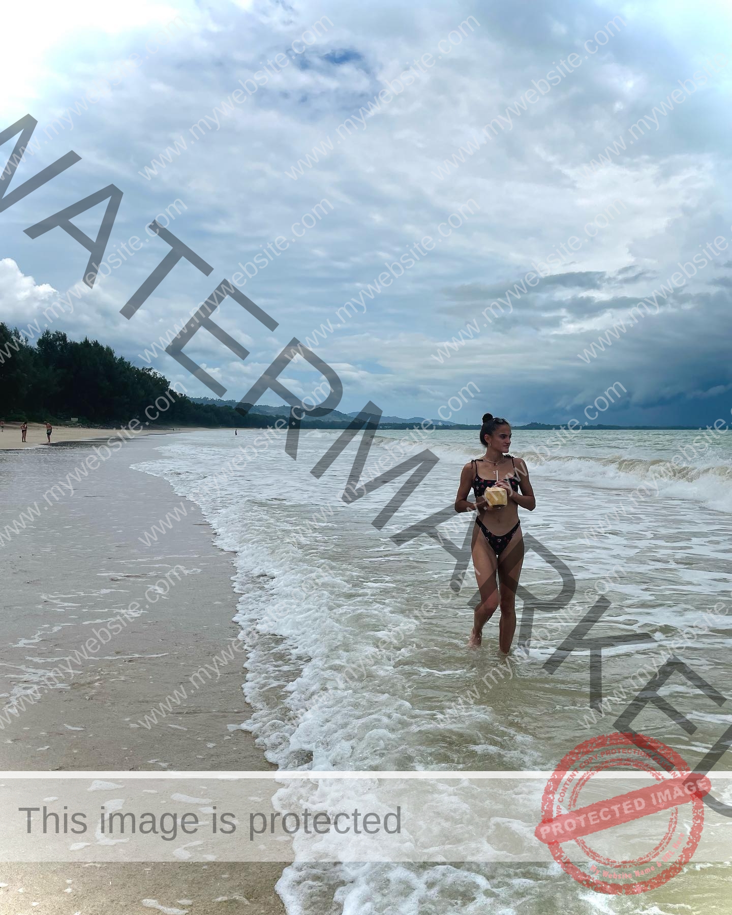 polina-tkalich-russia-p_a_tkalich-11003 Polina Tkalich, track and field star from Russia, walks in a black bikini along the ocean's edge on a sandy beach under clouds.
