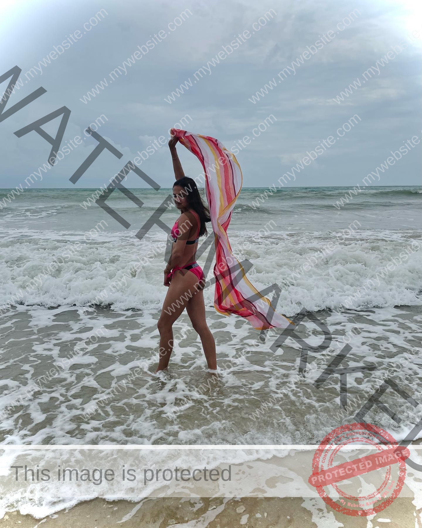 polina-tkalich-russia-p_a_tkalich-11004 Polina Tkalich, track and field star from Russia, stands in shallow waves in a pink bikini, holding a multicolored scarf overhead.