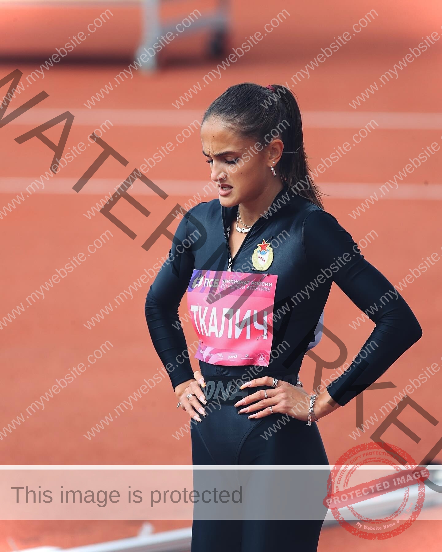 polina-tkalich-russia-p_a_tkalich-11142 Polina Tkalich, track and field star from Russia, stands on a track in a black tracksuit with race bib, eyes closed, looking focused.