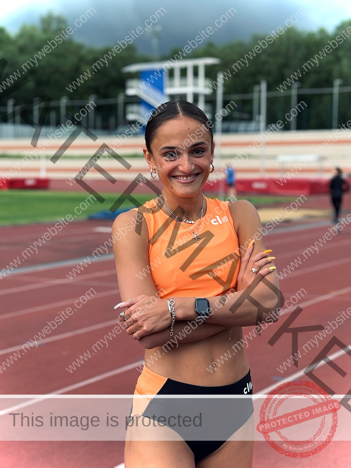 polina-tkalich-russia-p_a_tkalich-11244 Polina Tkalich, track and field star from Russia, in an orange crop top and black shorts stands smiling on a running track.