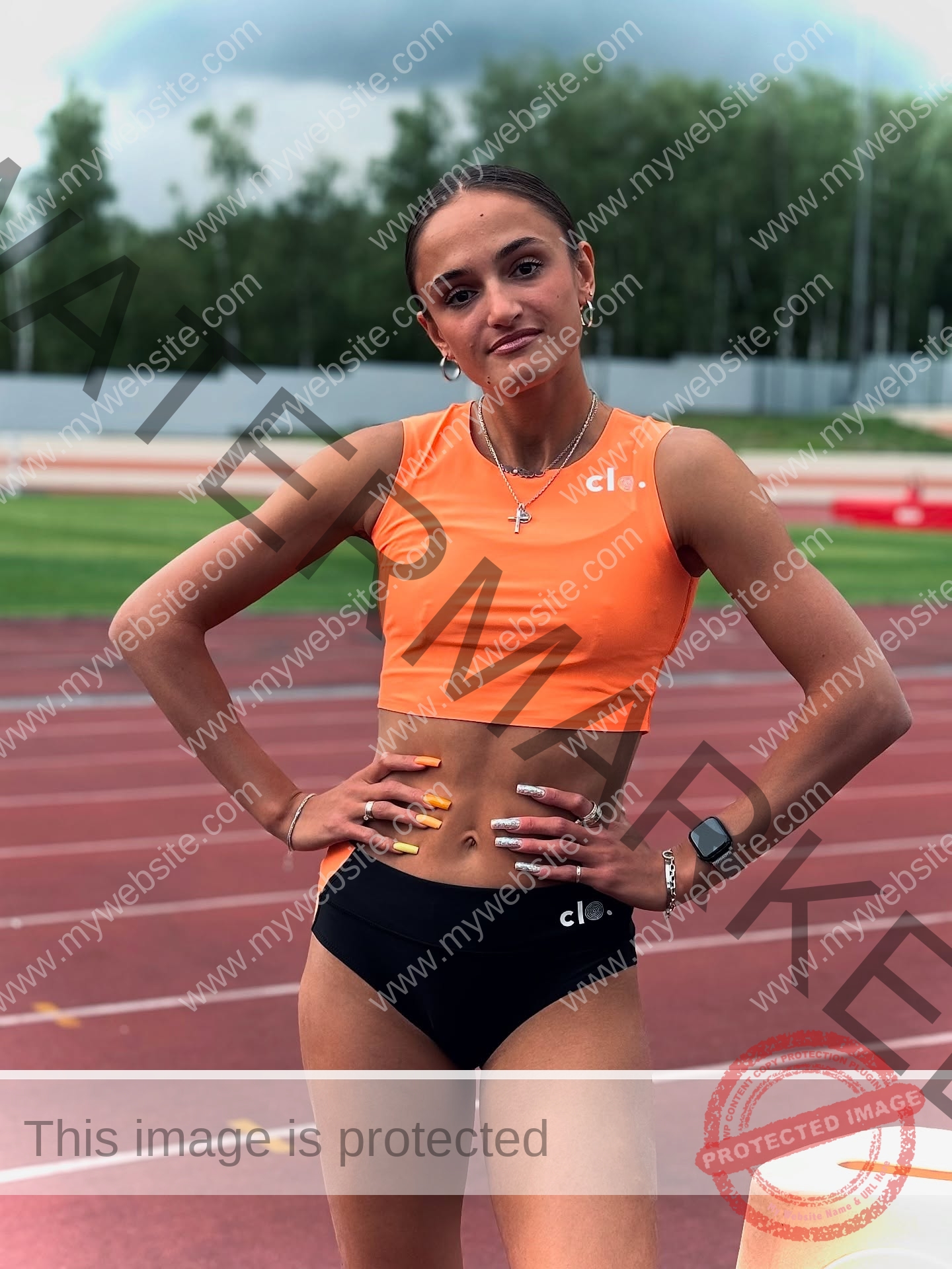 polina-tkalich-russia-p_a_tkalich-11246 Polina Tkalich, track and field star from Russia, wears an orange crop top and black shorts on a running track, hands on hips.