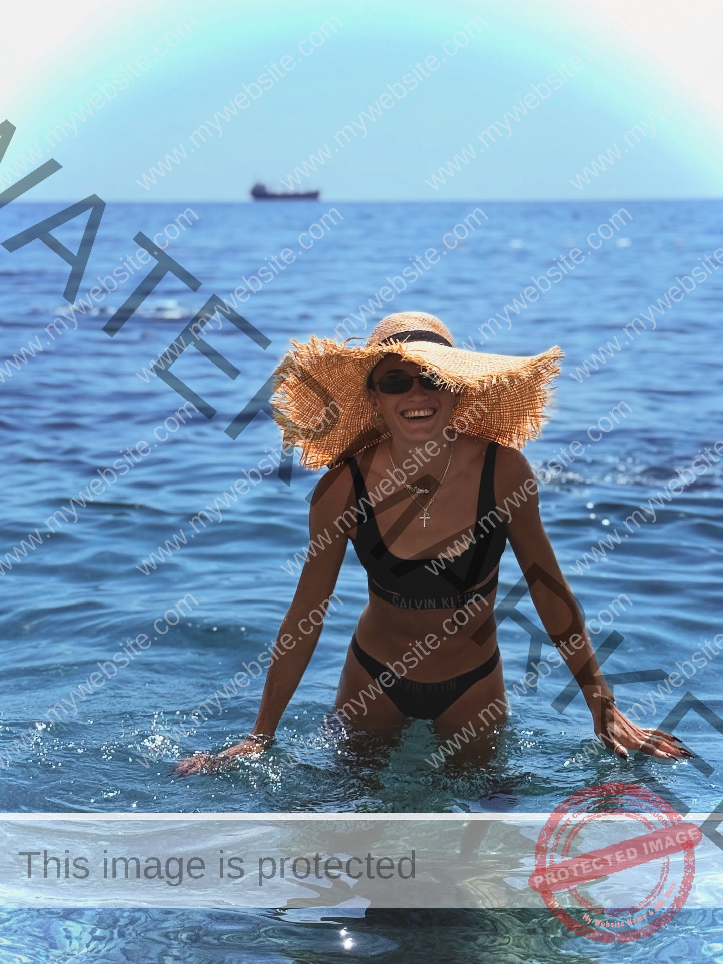 polina-tkalich-russia-p_a_tkalich-11321 Polina Tkalich, track and field star from Russia, wears a straw hat and black bikini, smiling in blue sea with ship on the horizon.